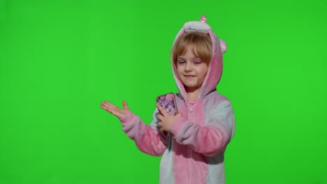 Child-girl-in-unicorn-pajama-using,-holding-smartphone,-pointing-at-something-with-hands,-copy-space