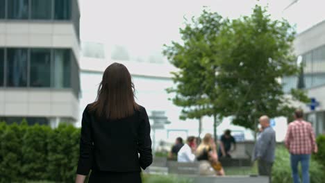 a woman with long brown hair walks away from the camera, in a modern urban setting