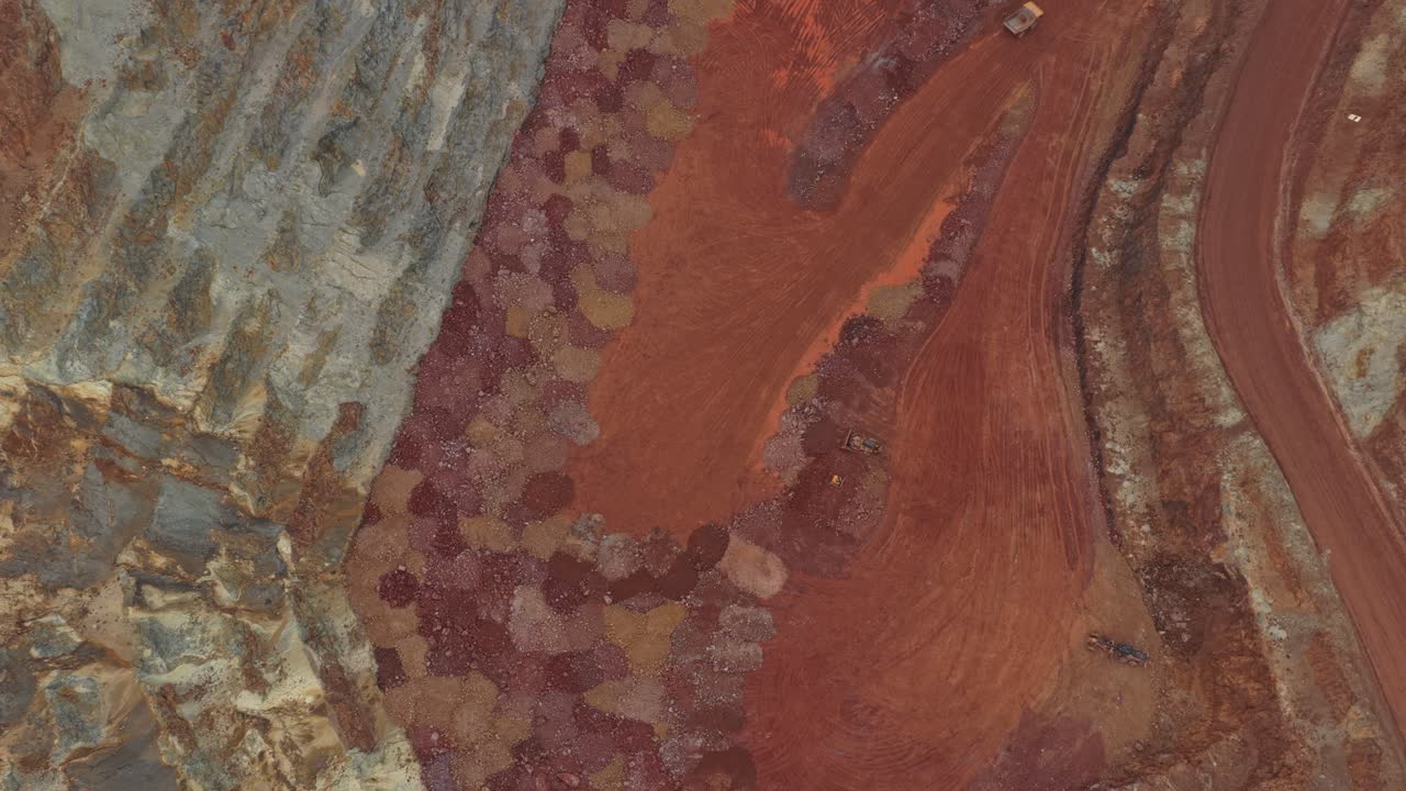Spettacolare vista aerea dall'alto di una vasta miniera di bauxite a cielo aperto. Grandi dumper guidano lungo strade sterrate tortuose nella cava.
