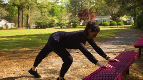 a young woman dressed in all black takes time to stretch before an outdoor workout at al local park