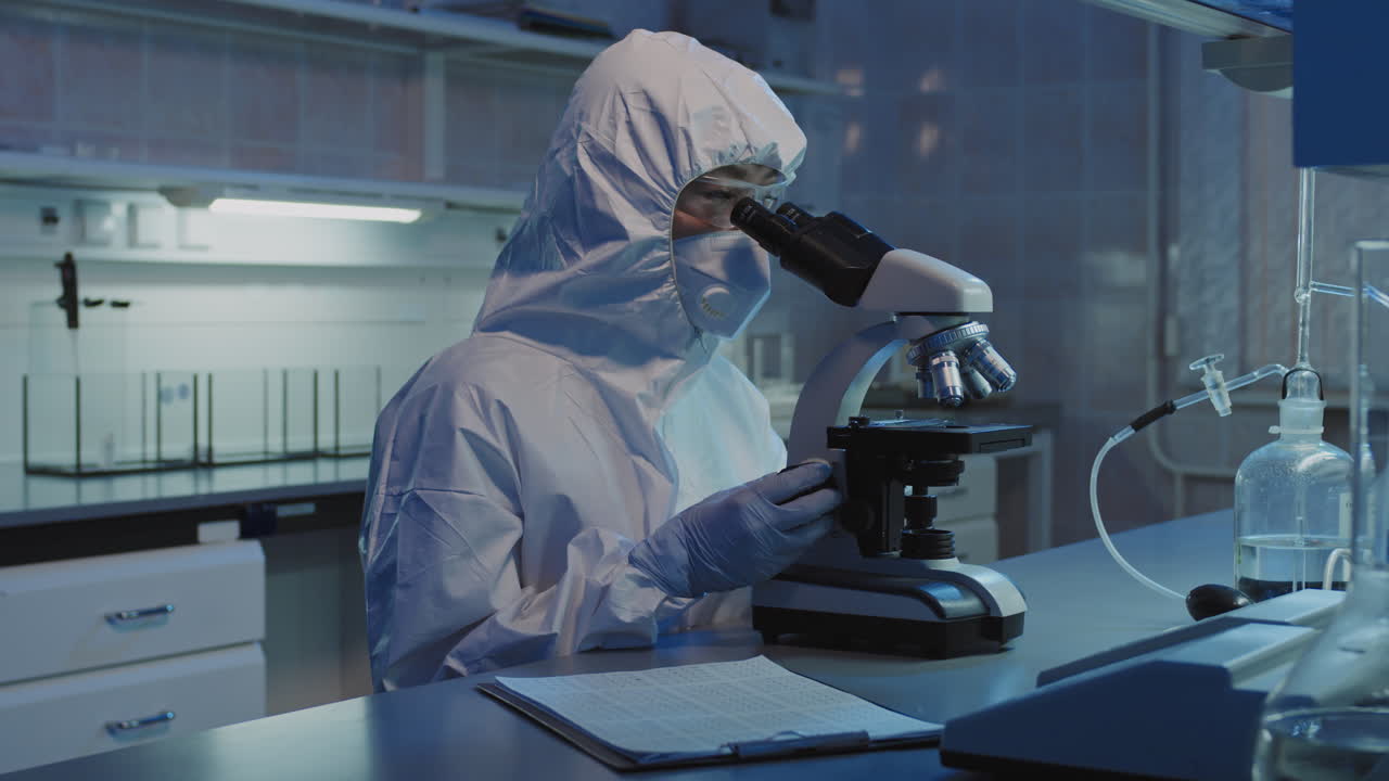 Epidemiologist in Protective Coveralls Using Microscope in Lab