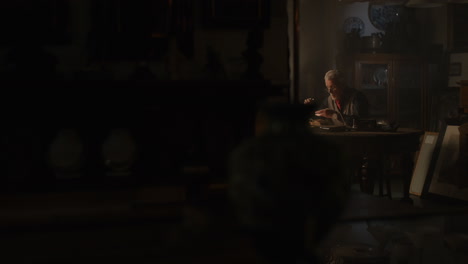older passionate man evaluates an old silver skull watch in his office at night