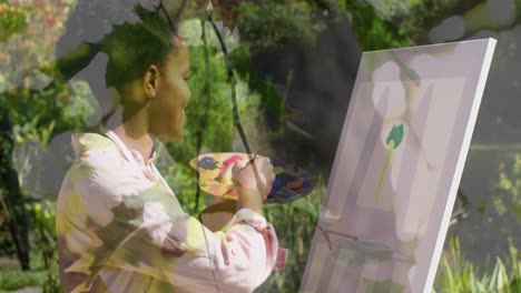 Animation-of-tree-over-african-american-woman-painting-on-easel-in-garden