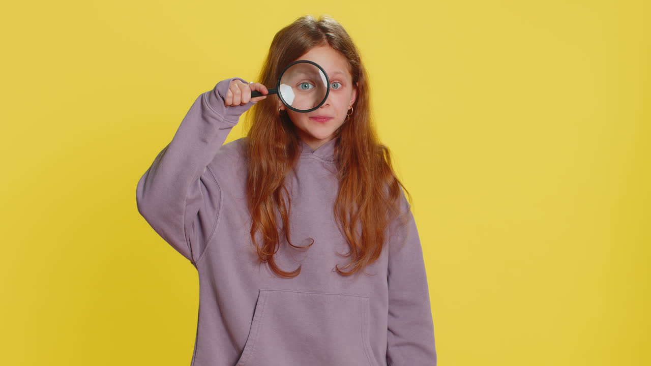 Child girl kid holds magnifying glass near face looking at camera with big zoomed eye analyzing
