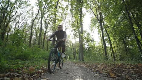 front view of man on bicycle with glasses riding away in the forest road. man on a mountain bike rides through the forest in summer sunrise.