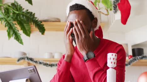 happy african american man wearing santa hat, using tablet for video call