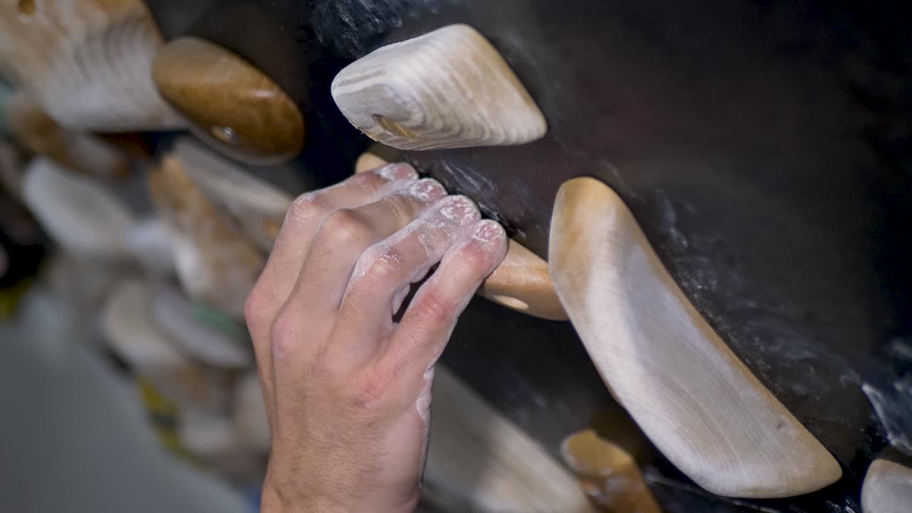 Slow motion close-up of chalked man's fingers and hands gripping onto wooden climbing hardwood block holds on home indoor rock climbing bouldering wall garage shed in Australia sports leisure activity