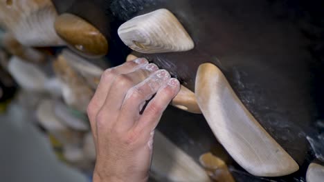 slow motion close-up of chalked man's fingers and hands gripping onto wooden climbing hardwood block holds on home indoor rock climbing bouldering wall garage shed in australia sports leisure activity
