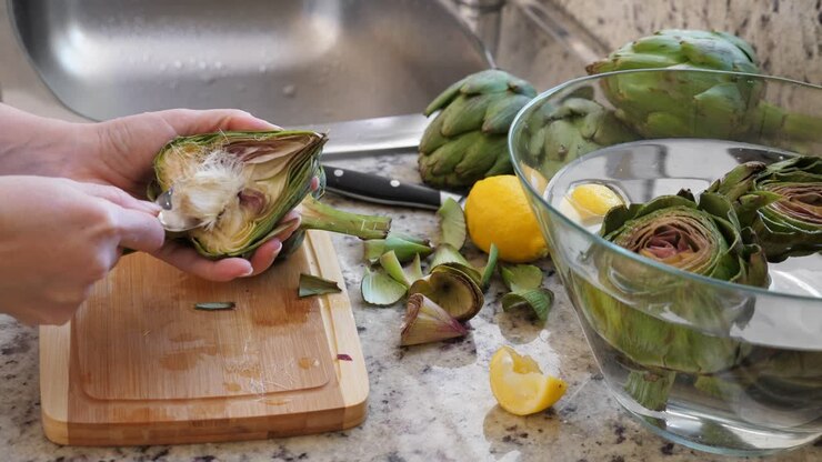 Woman cleaning heart of artichokes with spoon. Cooking process at the kitchen. Ready to prepare