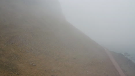 Cliff-with-road-on-misty-Icelandic-coastline,-aerial-drone-shot