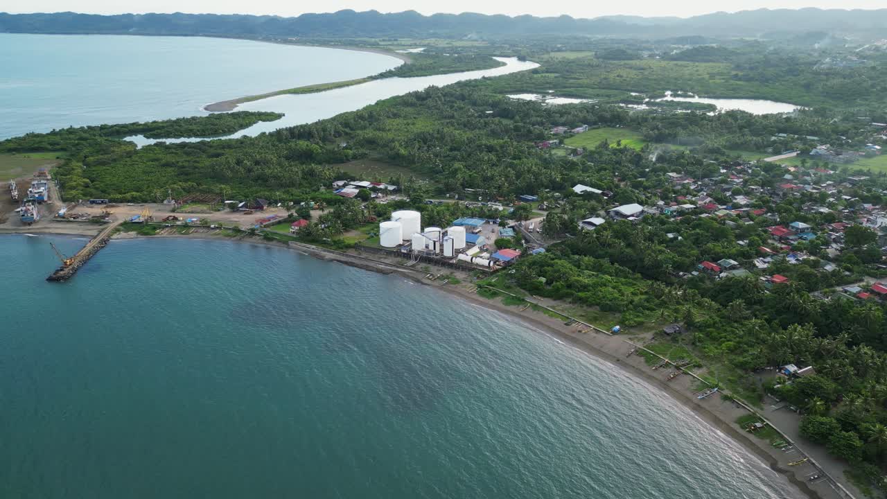 Panoramic aerial drone shot of fuel storage facility along the coast of a quaint, lush, tropical island during daytime. Virac, Catanduanes.