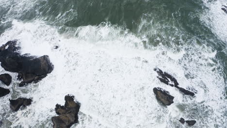 Aerial-View-Of-Ocean-Waves-Crashing-Against-Rocks-With-Water-Foam,-God's-Thumb-Oregon-Coast,-top-down-tilting-up