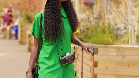 female tourist with camera on vacation in oxford uk exploring city walking along broad street pushing suitcase with wheels