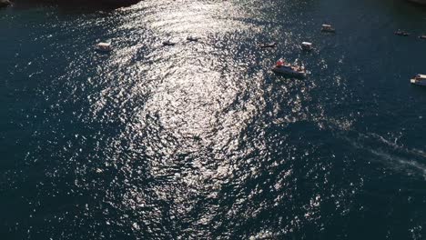 aerial drone shot tilting up revealing tonnara di scopello and spiaggia la tonnara in sicily, italy, passing over boats in the ocean during golden hour in italian summer (sicilia, italia)