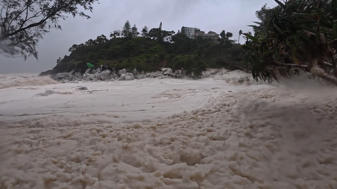 People Sitting On Shore Covered With Sea Foam Amidst Catastrophic Cyclone Alfred At Froggy Beach In Queensland, Australia. static shot