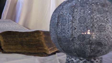 Historic-old-book-open-on-table-with-flickering-candle,-close-up