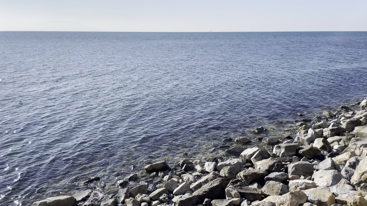 Beautiful coastal view featuring a rocky shore and shimmering blue sea under natural sunlight, ideal for nature, travel, and seascape themes