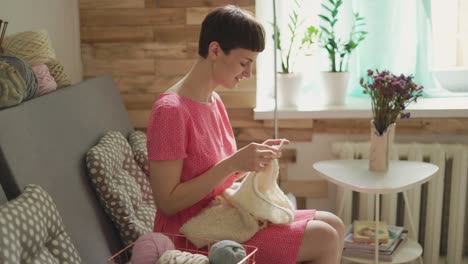 Smiling-woman-knitting-needles-woolen-clothes-on-background-window