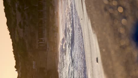 Olas-En-Cámara-Lenta-En-Una-Orilla-De-Playa-Pedregosa-Durante-El-Disparo-Vertical-Al-Atardecer