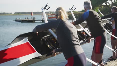 rowing team of four senior caucasian men and women lowering boat into river