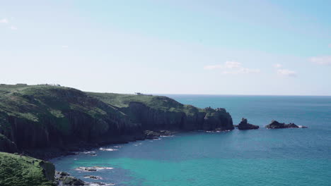 cliff on the rocky shoreline of land's end in cornwall, uk surrounded by turquoise blue sea - static shot