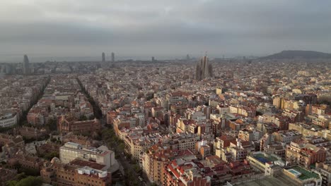 An aerial drone shot of Barcelona&#039;s cityscape with high and low-rise buildings as well as Sagrada Cathedral in the distance