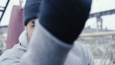 nahaufnahme eines gutaussehenden bärtigen kaukasischen mannes in grauem hoodie und boxen vor der kamera im freien einer verlassenen fabrik an einem bewölkten morgen