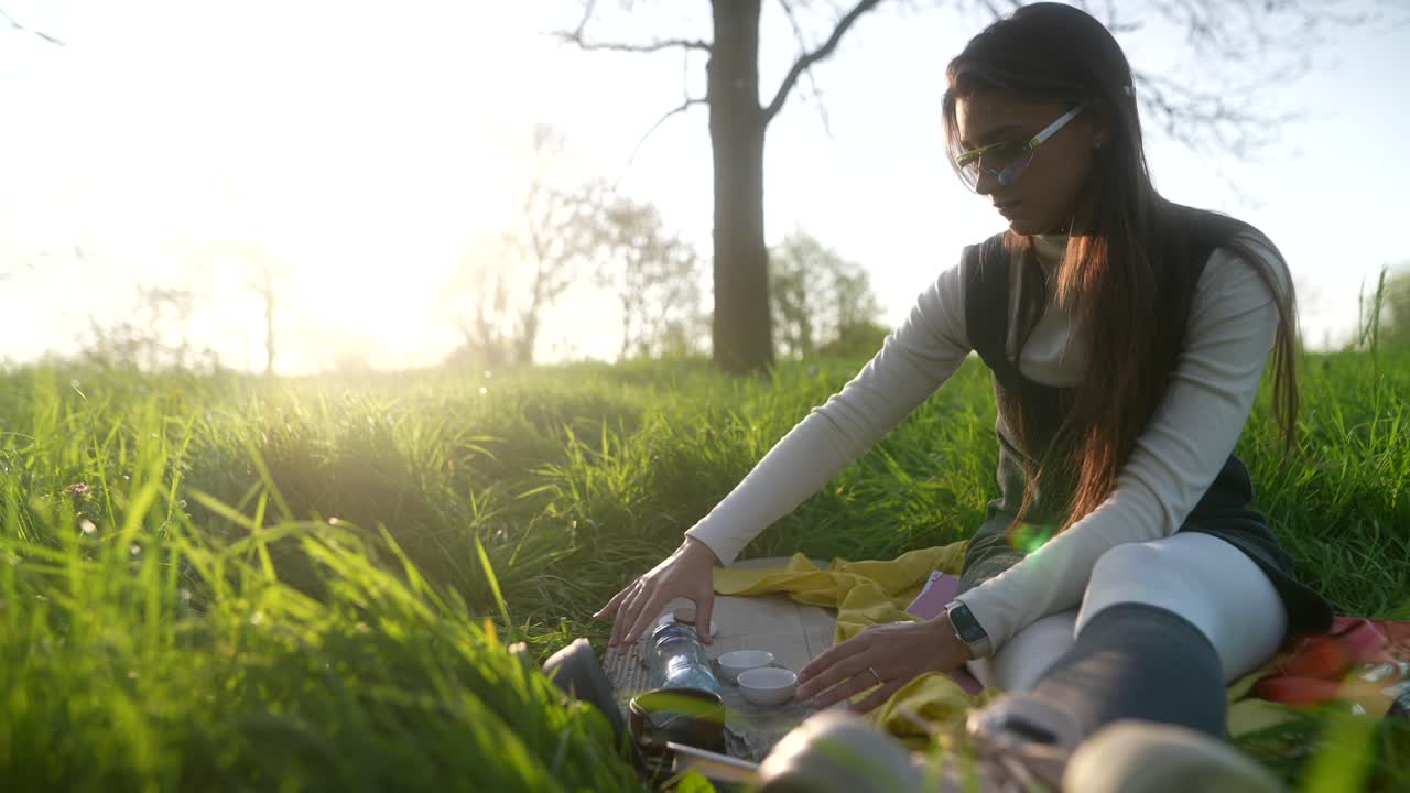 Woman enjoying a picnic tea ceremony in a park at sunset