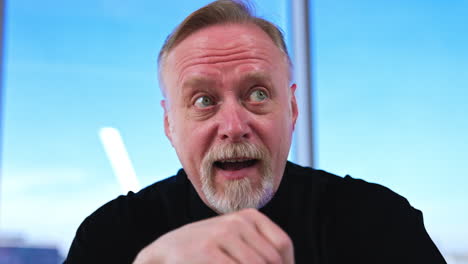 bearded mature caucasian man holding glasses in his hand. calm man bursting into laughter. close up.