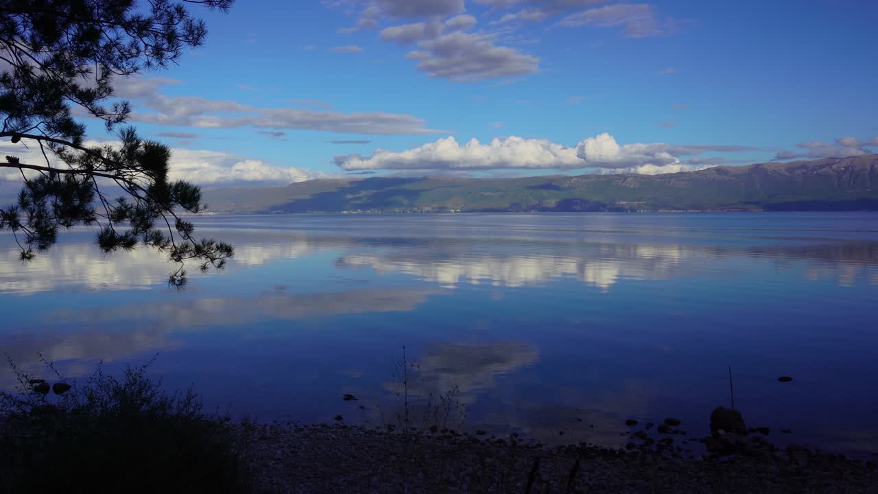 vista panorámica del lago ohrid con aguas tranquilas que reflejan nubes blancas y montañas al atardecer