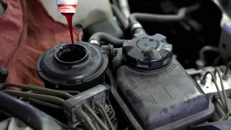 Mechanic-slowly-pouring-red-gloopy-power-steering-fluid-into-car-engine-in-garage-shop,-as-he-works-on-engine-of-old-BMW