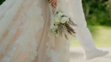 bride gracefully holds a white floral bouquet, her intricate lace gown flowing beautifully around her