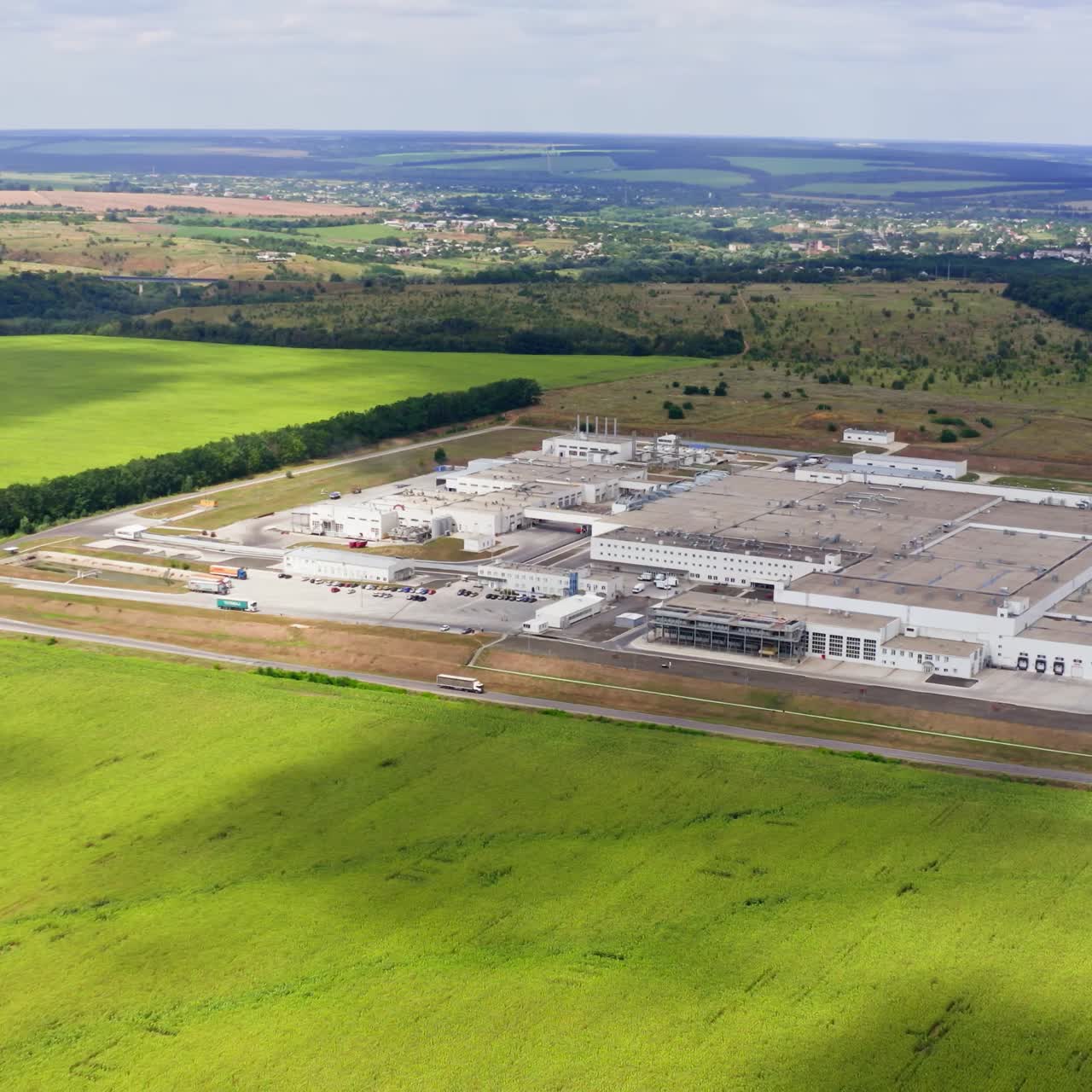 Modern industrial plant on field. Large factory among beautiful green nature. Agricultural center in the countryside. Aerial view