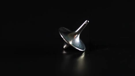 a shiny metallic top spins gracefully on a dark surface, showcasing balance and motion.