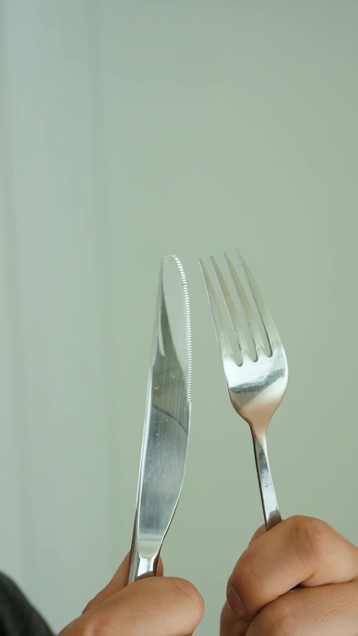 Close-up de um homem faminto segurando um garfo e uma faca, simbolizando apetite, à espera de comida, hora da refeição, almoço, jantar, desejos e hábitos alimentares diários.