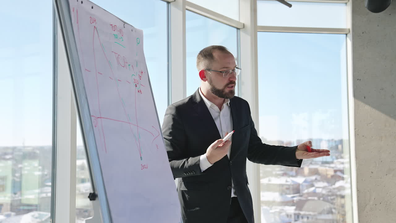 Speaker performs a speech in front of the colleagues. Businessman gives a speech and shows the curves at the chart.