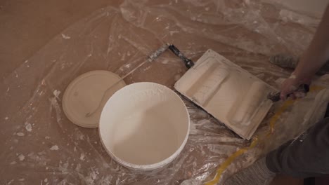 person taking paint with roller for wall white painting