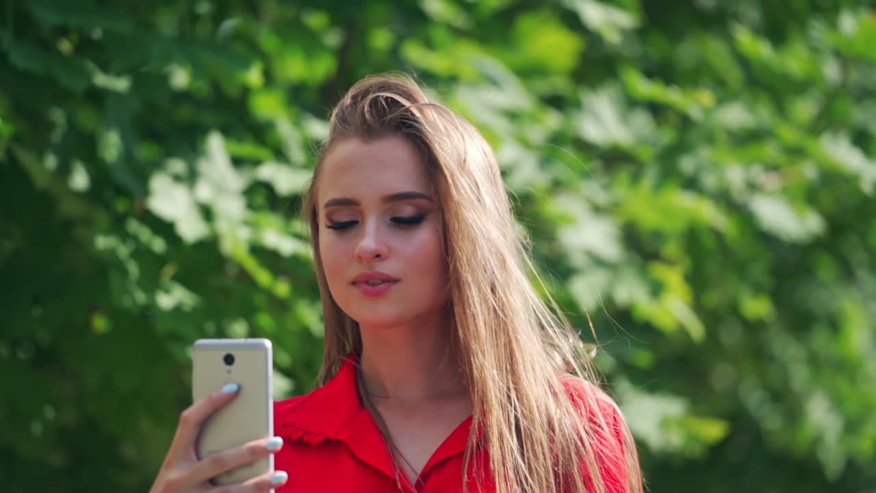 Beautiful woman doing selfie. Gorgeous young female in red dress photographing herself on the mobile phone outdoors.