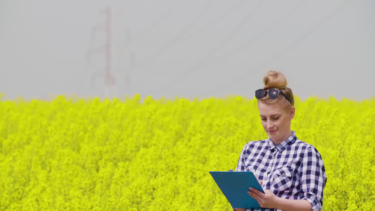 Young female farmer takes notes near blooming rapeseed