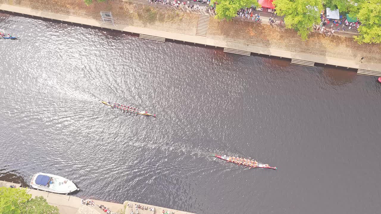 Aerial top-down view of competitive rowing crews gliding along the River Ouse in York, England, with riverside walkways, spectators and moored boats
