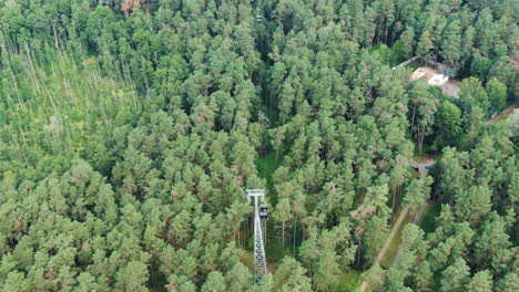 Cable-cart-pole-with-moving-carts-surrounded-by-dense-conifer-forest-in-Druskininkai,-aerial-view