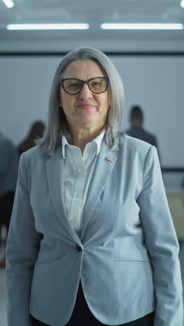 Portrait-of-mature-woman,-United-States-of-America-elections-voter.-Businesswoman-stands-in-a-modern-polling-station,-poses-and-looks-at-camera.-Background-with-voting-booths.-Concept-of-civic-duty.