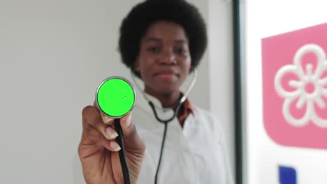 mujer profesional médica afroamericana que muestra un estetoscopio con pantalla verde. mujer médica sosteniendo un estetoscópio con pantalla verde hasta la cámara. pantalla verde en el estetoscopio