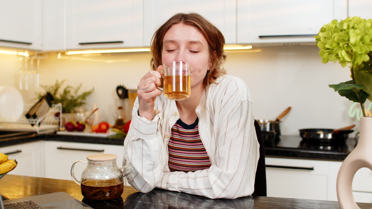 Giovane donna che beve tè caldo alle erbe nella cucina di casa, godendosi una pausa dietetica tranquilla e un riposo sano e accogliente.