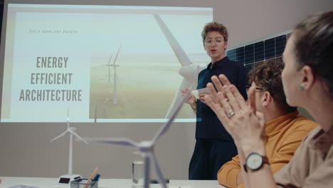 young businesswoman pointing at slides on projection screen, giving presentation about energy efficient architecture on team meeting in the office during night, working in renewable energy company