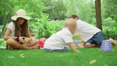 three children playing with toys in park. toddler lying on green grass outside