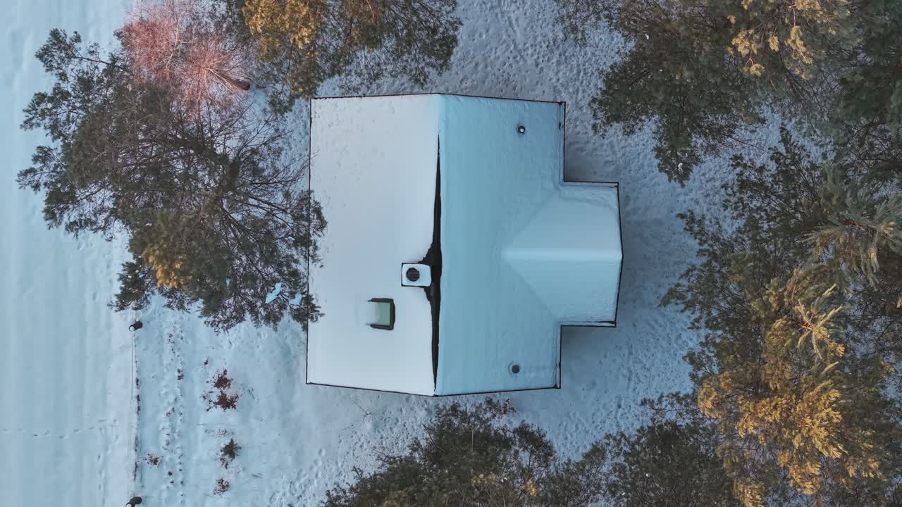 Aerial view showing house roof covered in winter snow surrounded by trees. rising shot