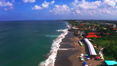 big foamy waves washing upon sandy beach with resorts in canggu, bali