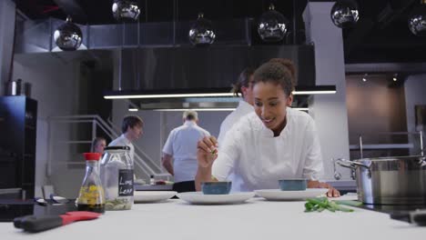 chef afroamericana vestida con ropa blanca en una cocina de restaurante condimentando comida
