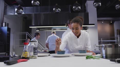 african american female chef wearing chefs whites in a restaurant kitchen seasoning food